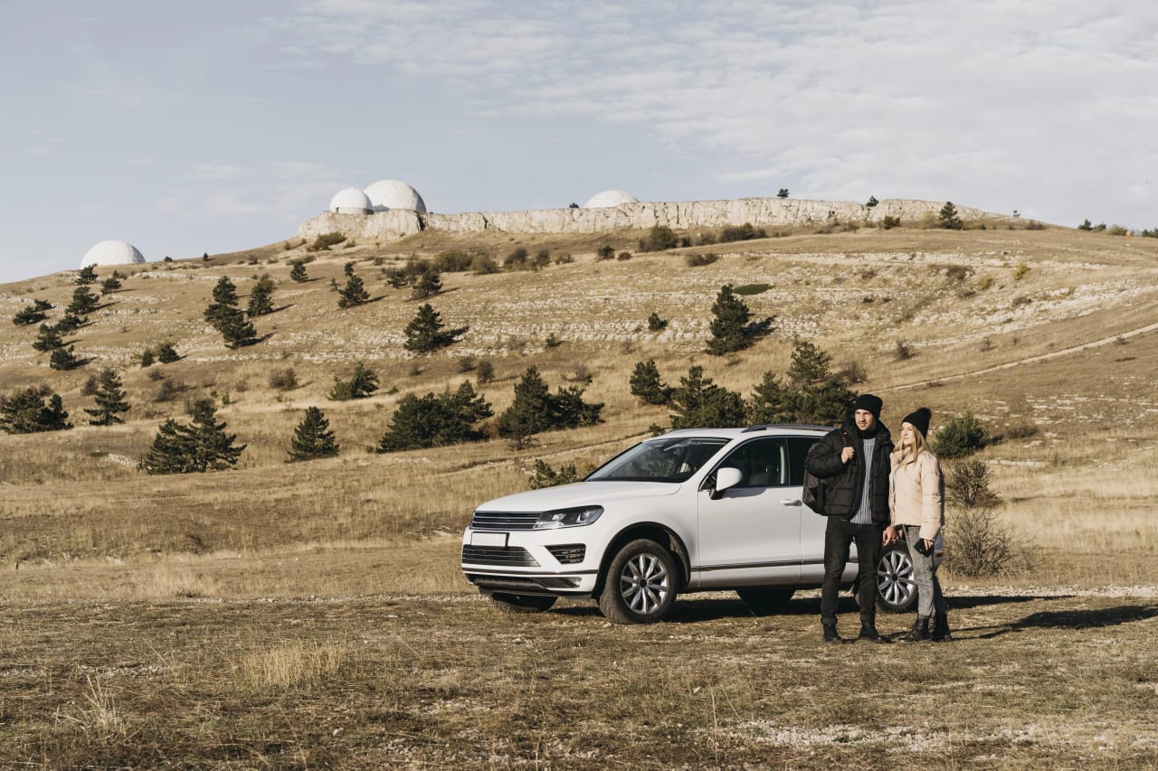 Two people beside a white SUV on an open hillside